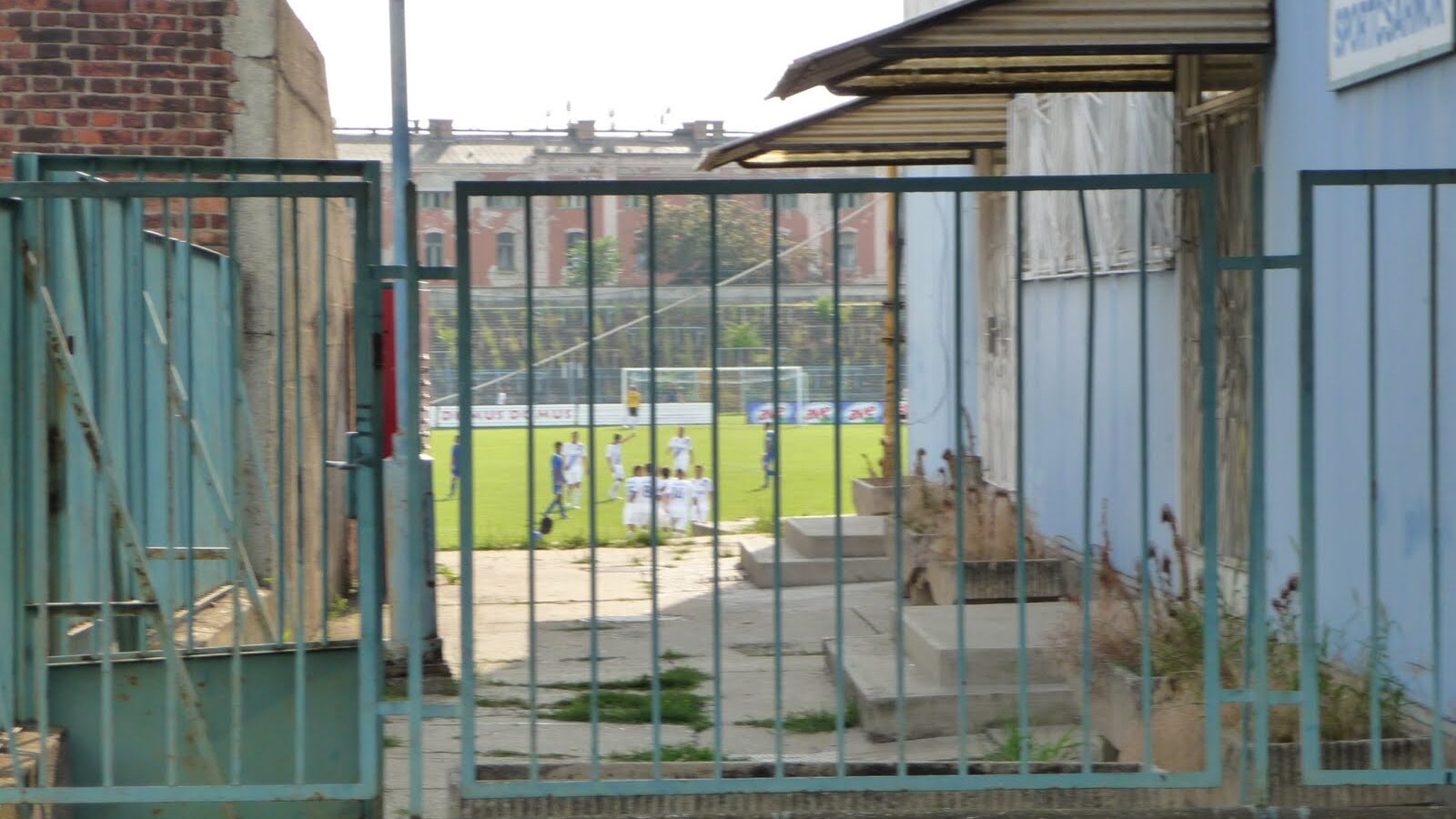 A small area of the pitch seen through metal railings outside a football stadium